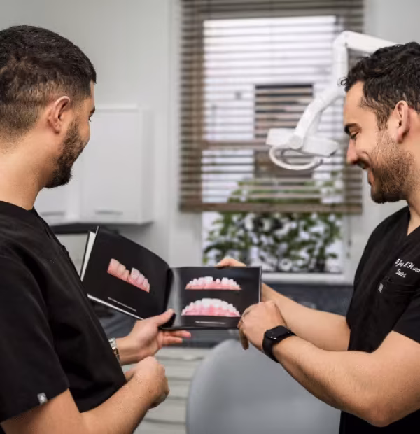 Two dentists in black scrubs smiling while reviewing a portfolio of Composite Bonding before and after photos in a modern dental surgery.